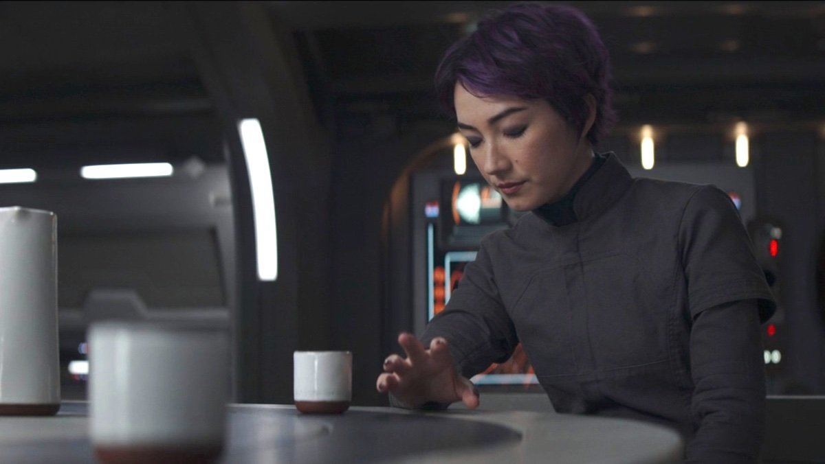 Sabine Wren at a table with her eyes closed trying to move a mug with the Force on Ahsoka