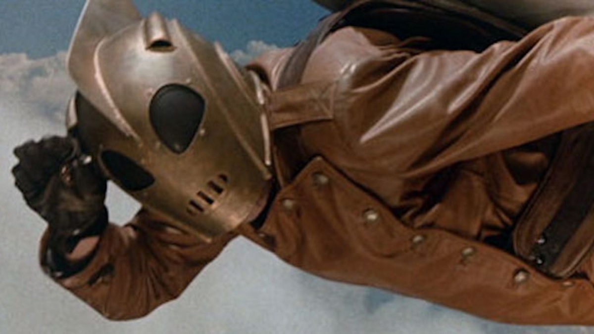 The Rocketeer salutes while flying in the sky.
