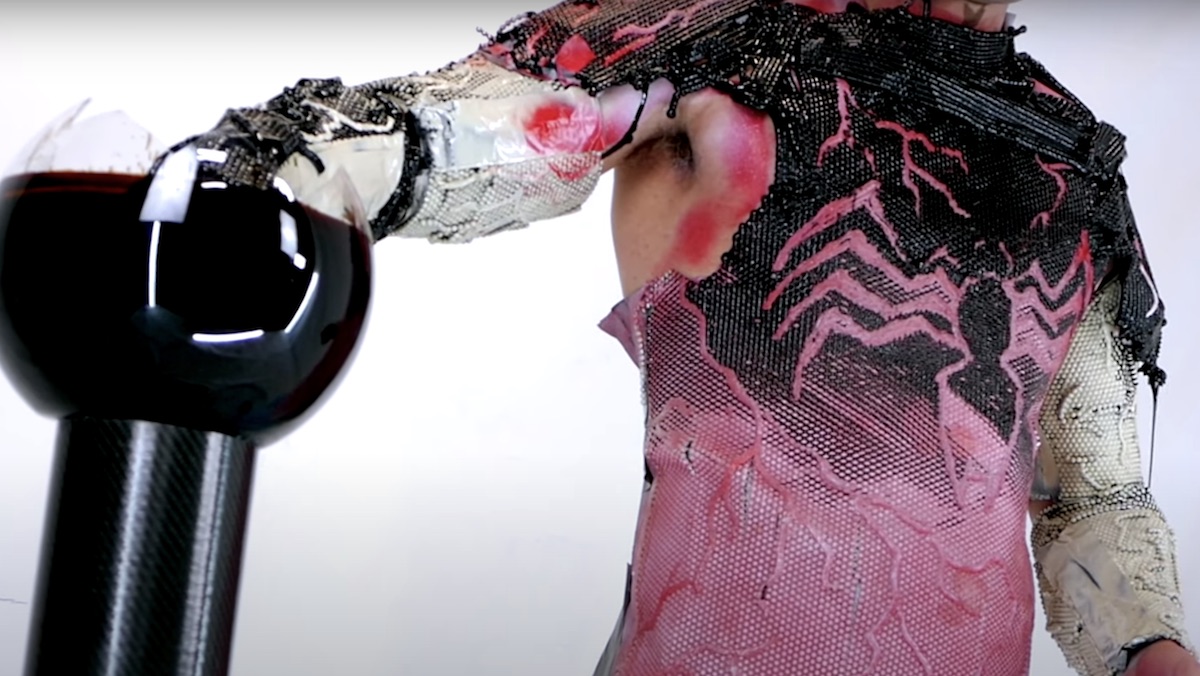 A man with his hand in a bowl of ferrofluid that creates a life-like Venom costume he's wearing