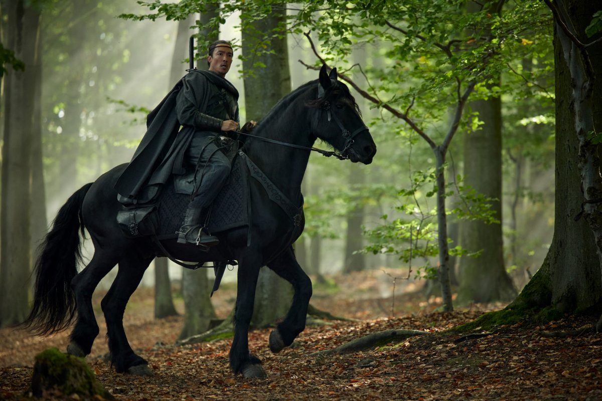 Lan Mandragoran riding Mandarb in a wooded area in The Wheel of Time season two